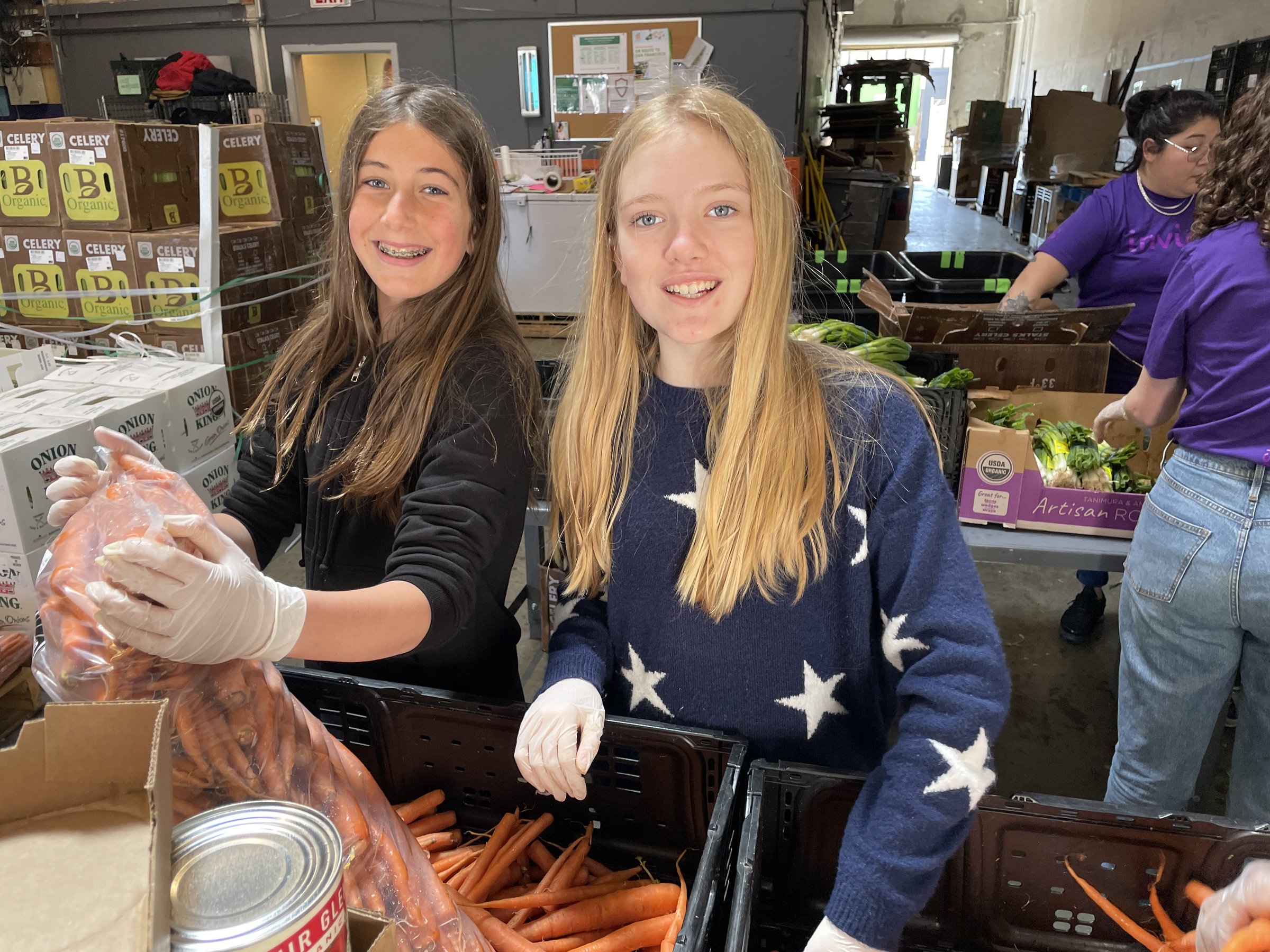 Two La Scuola students in gloves packing carrots at a community food bank