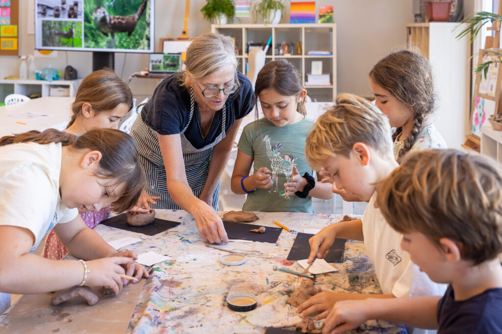 A teacher and children shaping clay together at a work table in the atelier