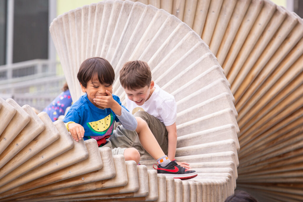 Two young children laughing together on a curved wooden play structure