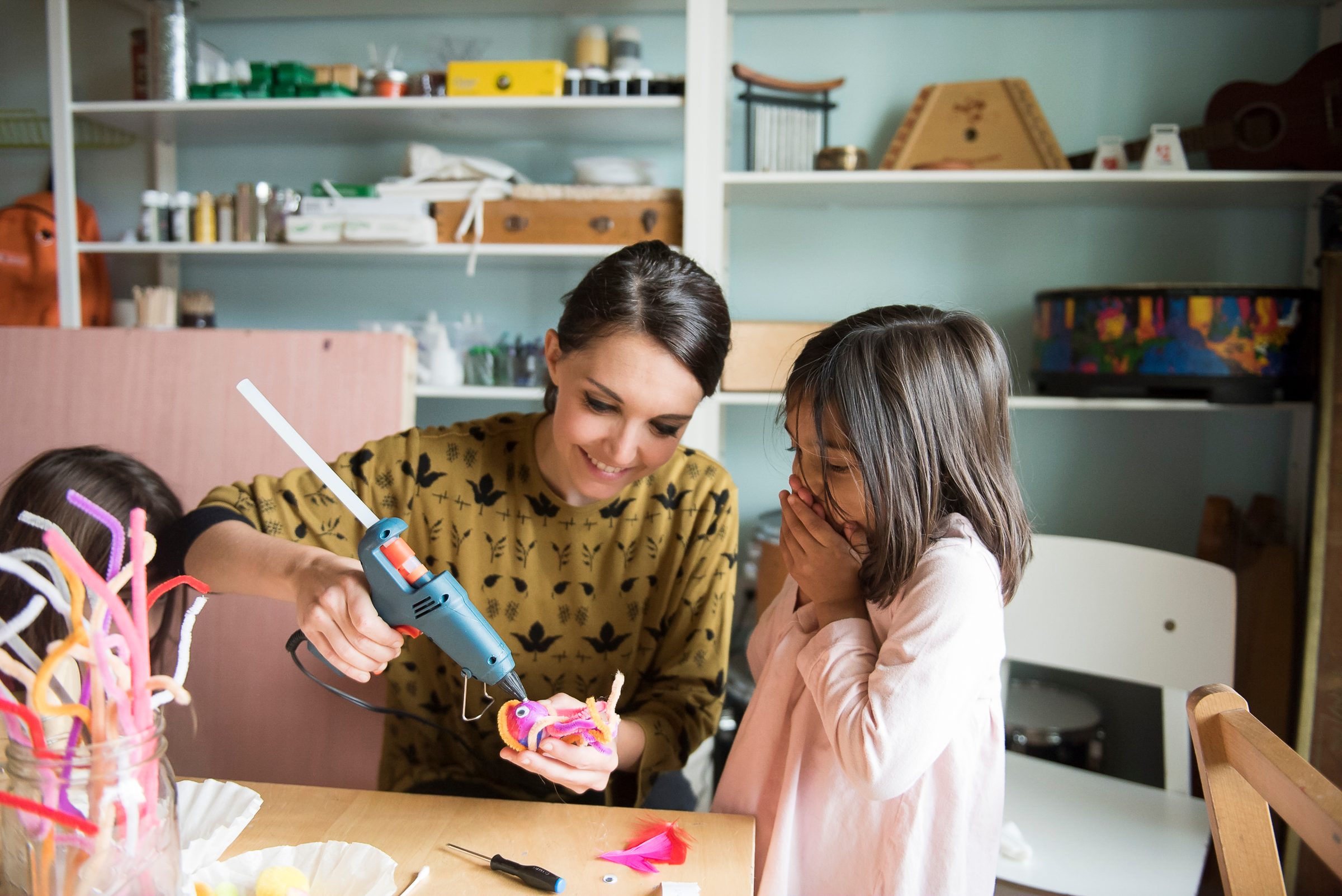 A teacher using a glue gun on a sculpture while a child watches closely