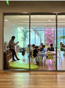 View through glass doors into a classroom where students work at low tables