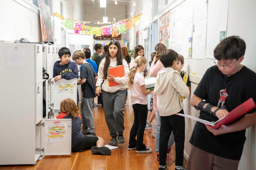 Students gathered in a hallway of lockers, reading and comparing their work