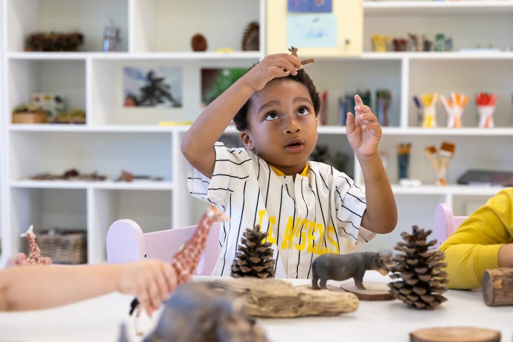 Preschooler gesturing over a table of animal figures, pine cones and driftwood