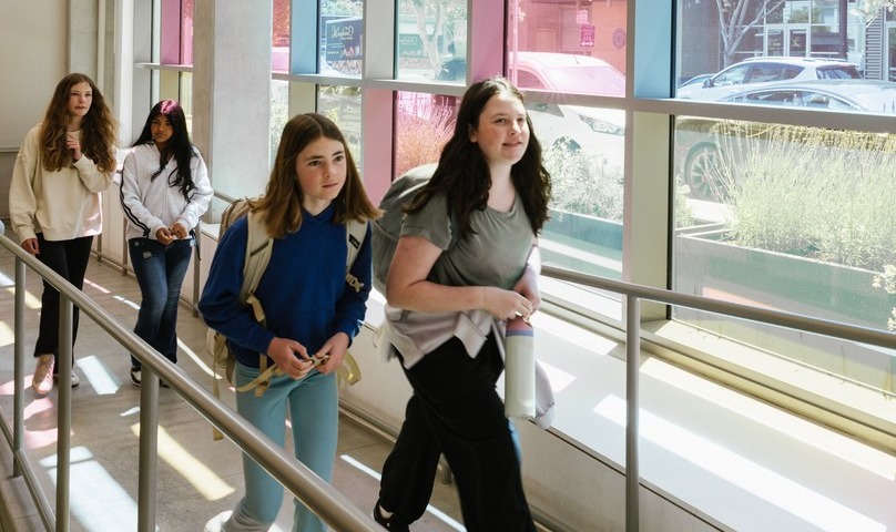 Students walking along a corridor lined with panes of colored glass