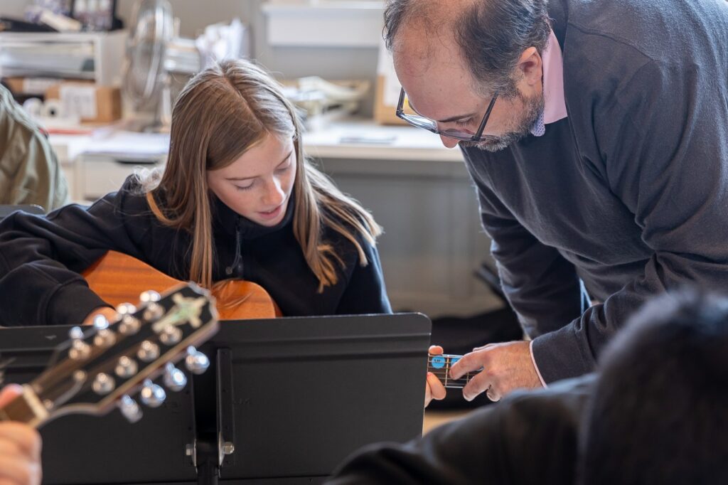A teacher leans in to help a student practicing guitar