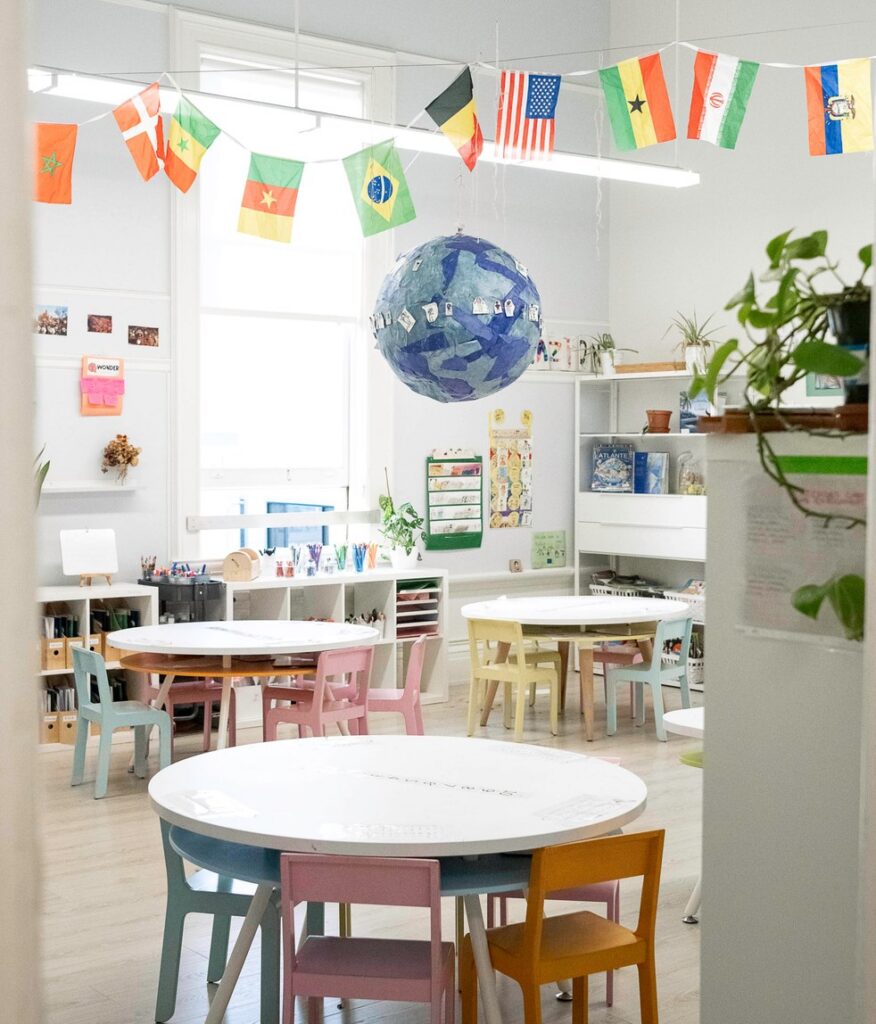 A La Scuola classroom with a paper globe and a string of international flags over the tables