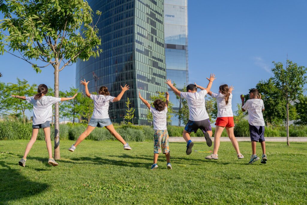 Children jumping for joy on the lawn in front of Milan’s towers